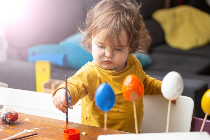 Toddler girl painting egg at table