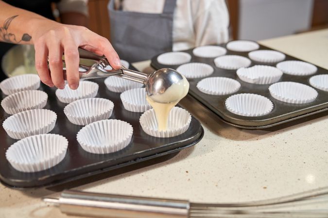 Unrecognizable parent filling cupcake mold near kid
