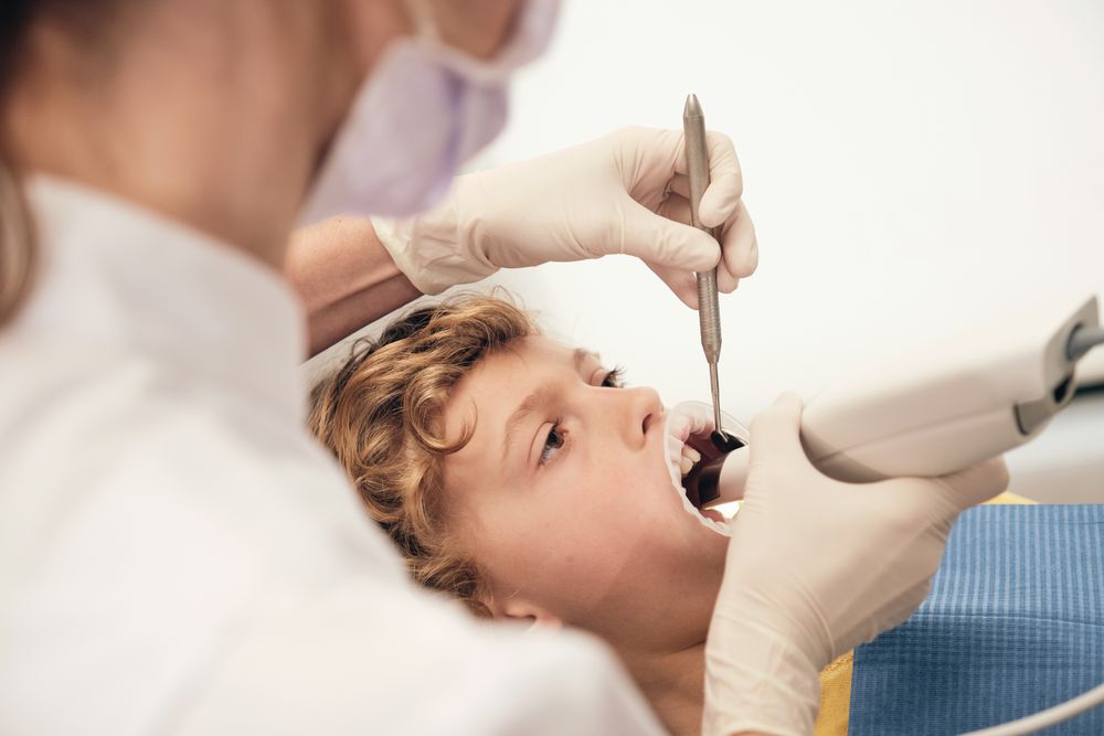 Kid lying on chair with opened mouth while unrecognizable stomatologist treating teeth