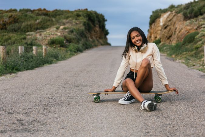Woman sitting on longboard on asphalt road