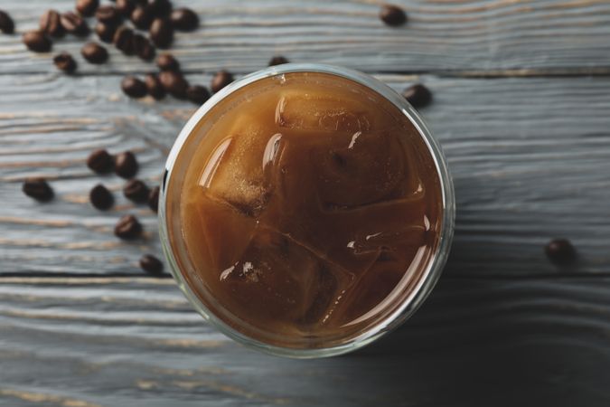Glass of ice coffee on wooden background. Coffee seeds