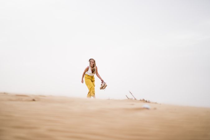Happy woman holding shoes in desert