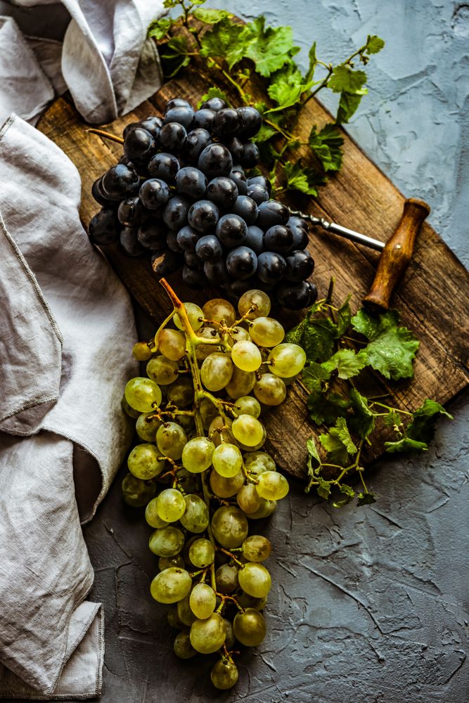 Top view of grapes on board with wine opener with kitchen towel
