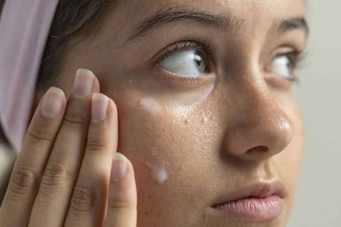 Macro of a woman applying a treatment for milia or clogged pores under her eyes