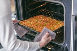 Crop woman putting homemade pizza in oven