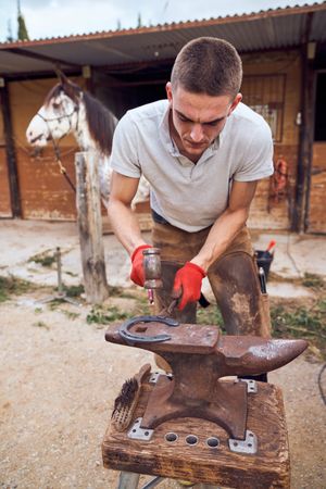 Blacksmith working on the anvil changing the horseshoe to a paw with tools