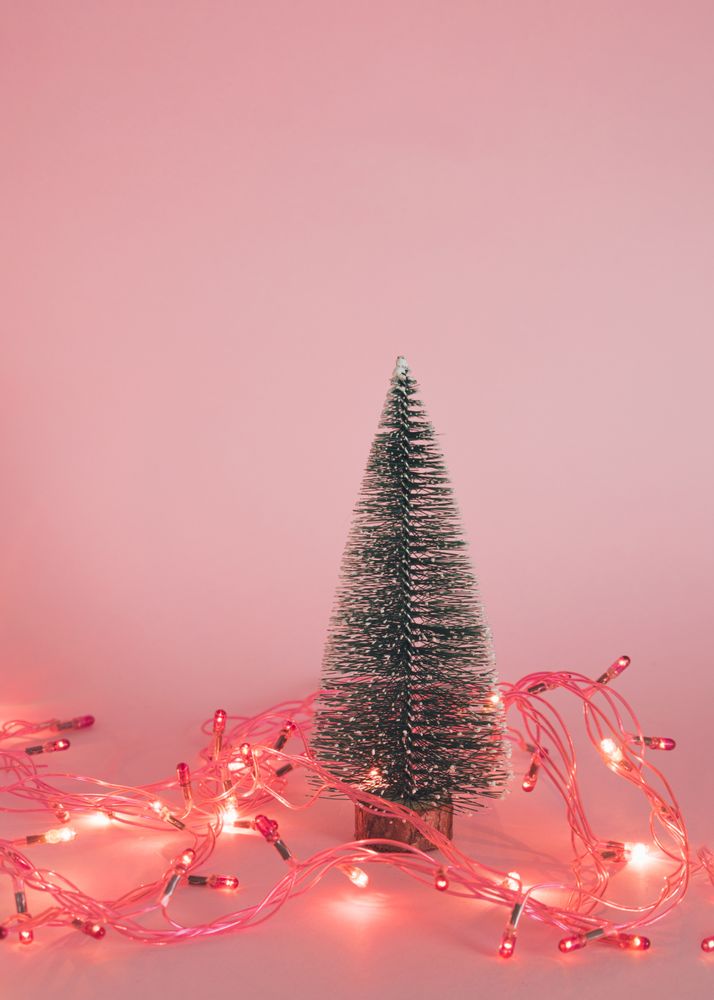 Christmas tree surrounded by fairy lights on pink background