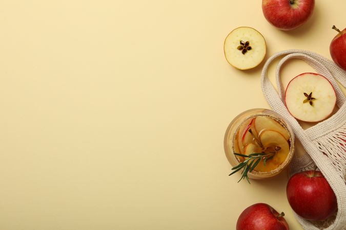 Glass of apple cider and apples in bag on beige background, space for text
