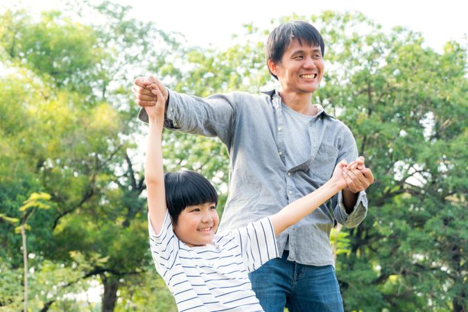 Father holding small son’s arms up in the air in public park