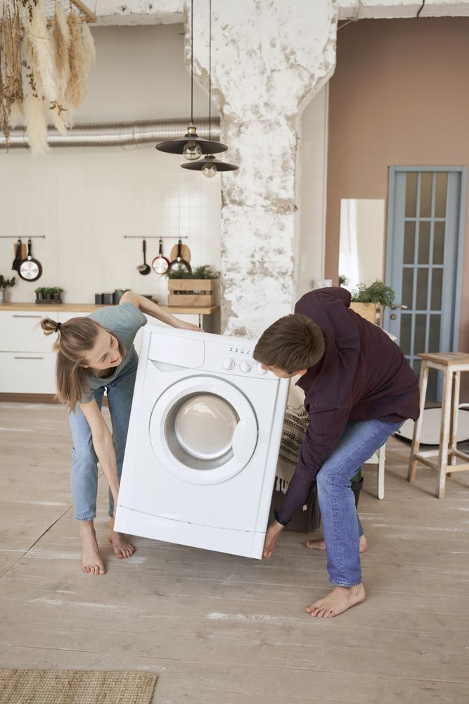 Enthusiastic couple carrying washing machine into new kitchen