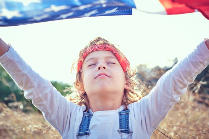 Calm preteen boy with raised hands and waving American flag