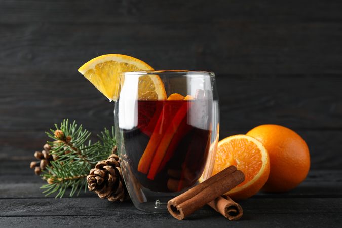 Glass of tasty mulled with orange on decorated background, space for text