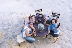 Aerial view of a group of friends sitting around a table holding beers with copy space