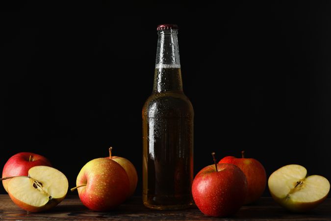 Composition with cider and apples on wooden table against dark background