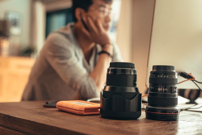 Camera lenses sitting on desk with blurry man in background