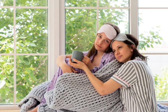 Mother comforting her daughter at home by a sunny window.