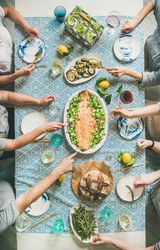 Group of people at blue patterned table serving themselves fish, and vegetable side dishes