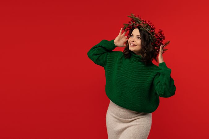 Woman in Christmas wreath looking up joyfully against red background.