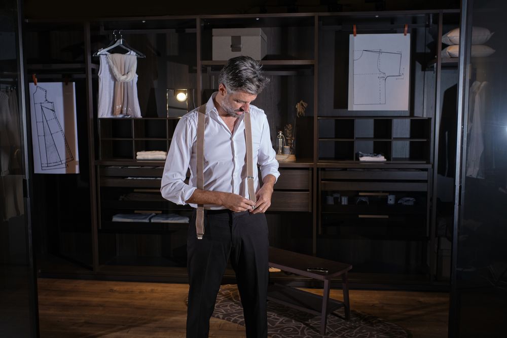 Confident gray haired man putting on suspenders for trousers in
