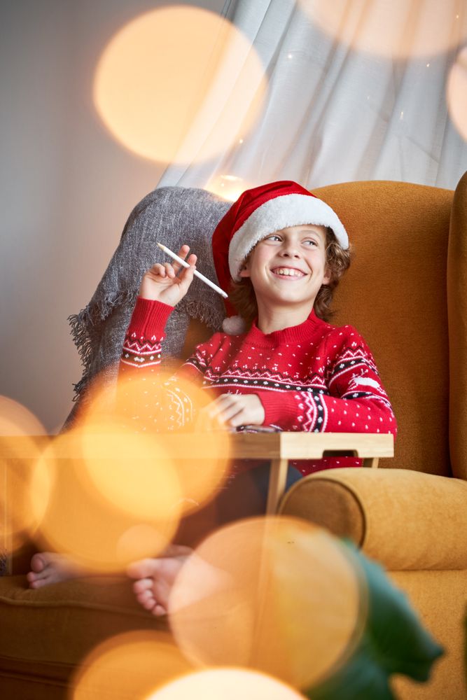 Cheerful boy in Santa hat drawing at home
