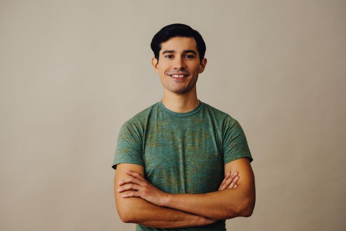 Happy Hispanic male standing in neutral room with arms crossed