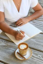 Crop woman writing in notepad while sitting in outdoor cafe with