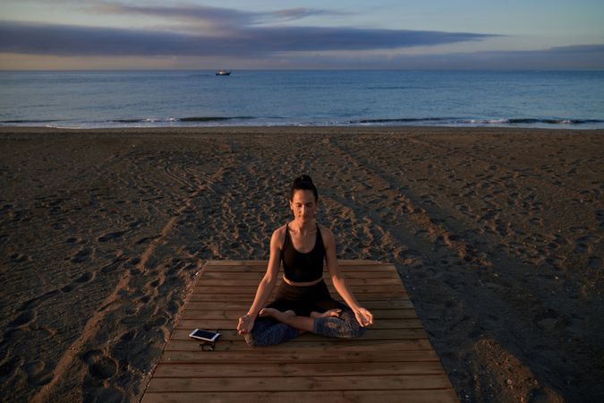 Peaceful Hispanic woman practicing lotus pose on seashore
