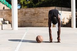 Black sportsman stretching on basketball court
