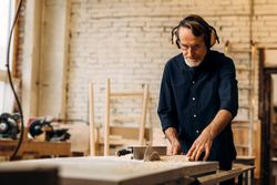 Older male in hearing protecting working on electric saw