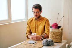 Man drinking hot tea during knitting
