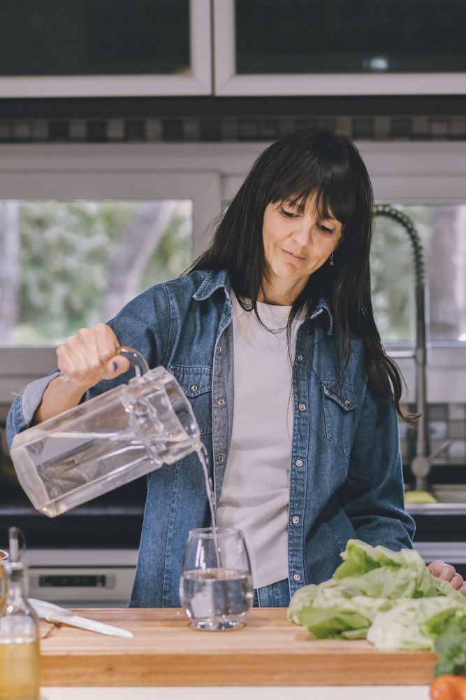 Woman pouring water in her kitchen. Vertical shot