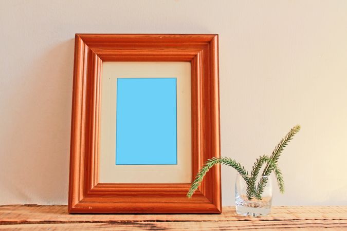 Rectangular wooden picture frame on wooden desk with branch in glass mockup