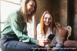 Two women smiling at something on a smartphone screen beXzy6