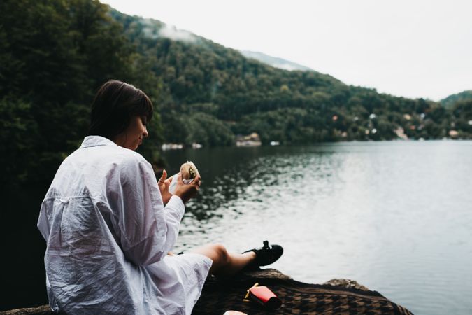 Woman eating hamburger near lake and mountains