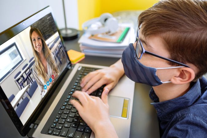Teenager with face mask listening to her teacher on video call