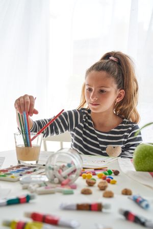 Girl choosing paintbrushes at table