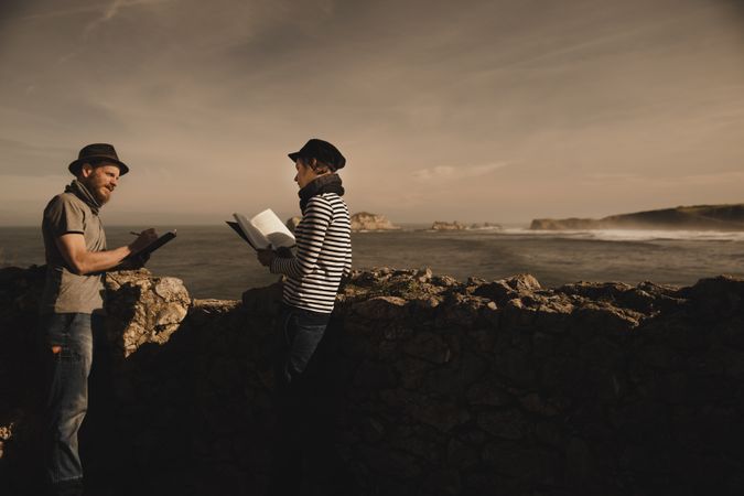 Man near woman with books near stones on shore