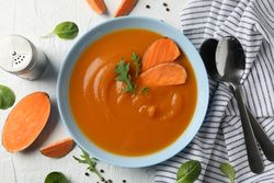 Sweet potato soup on table with kitchen towel, salt pepper and spoons