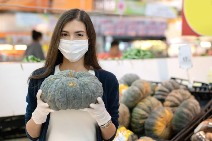 Woman in surgical mask and gloves picking square in produce aisle