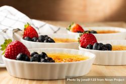 Side view of ramekins of creme brûlée with berries on wooden table 41z9Db