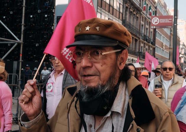 Mexico City, Mexico - February 26th, 2022: Older man in hat holding pink flag joining protestors