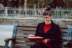 Young woman reading book on bench in park