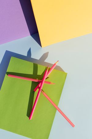 Pink pencils on green book, in space of geometric shapes.