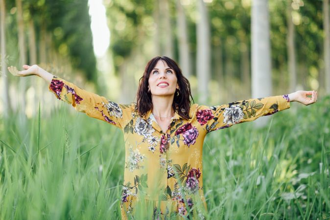 Smiling brunette female looking up in field of tall grass with outstretched arms