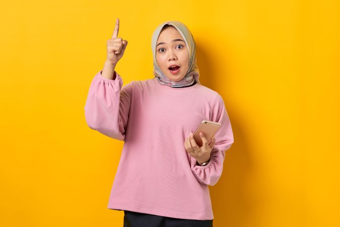 Shocked Muslim woman on the phone and pointing upwards with smart phone