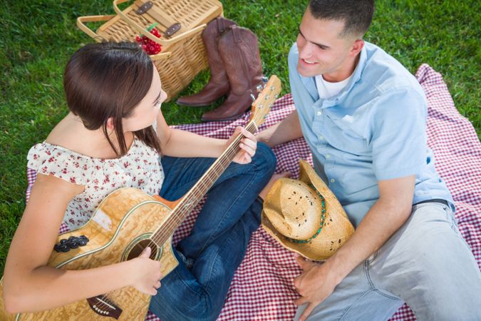 Young Adult Female Playing Guitar with Male In The Park.