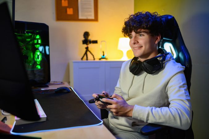 Concentrated happy young man sitting before monitor and playing games with joystick