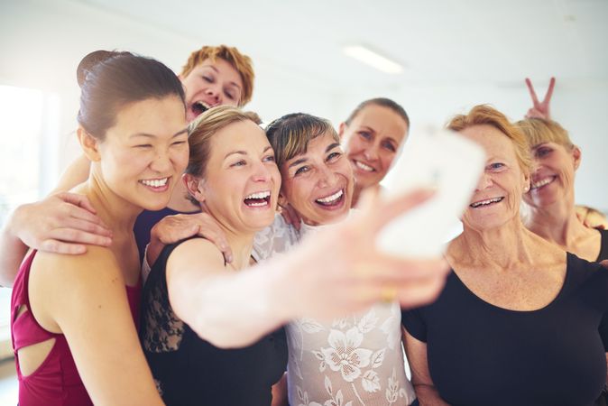 Group of laughing women pose for selfie in bright dance studio