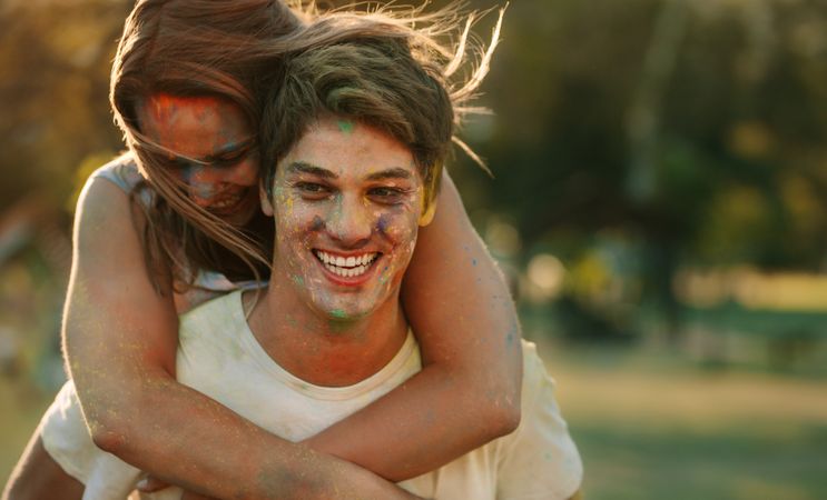 Smiling woman piggy riding on a man while playing holi in a park