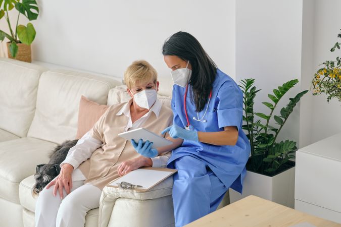 Physician sharing tablet with senior patient on couch at home